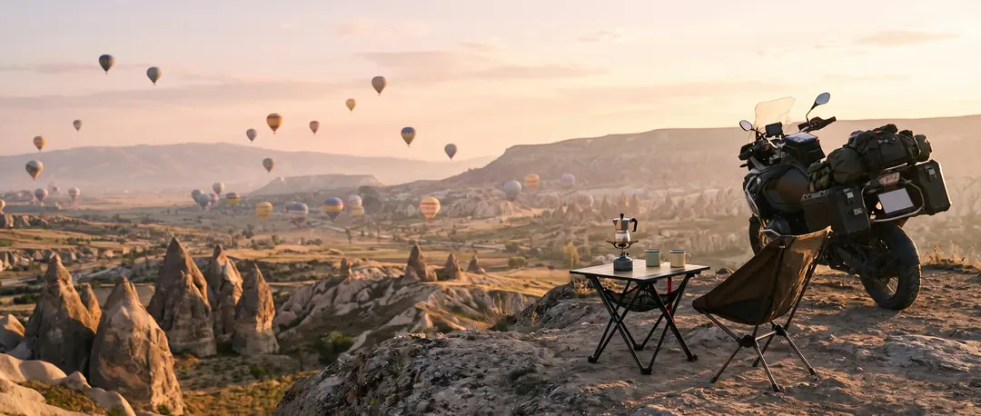 Kapadokya'da gün doğarken balonların ve peribacalarının karşısında motosikletin yanında üstünde kahve takımı olan KVOX Axis Ultra motosiklet masası